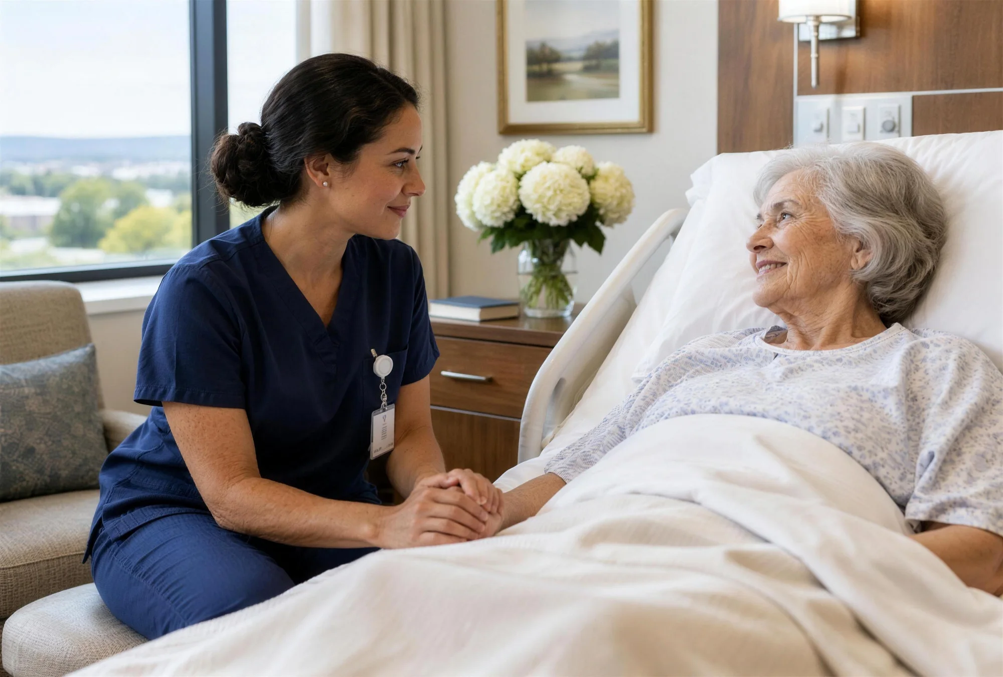 Certified nursing assistant holding the hand of a smiling older woman resting in a private hospital suite